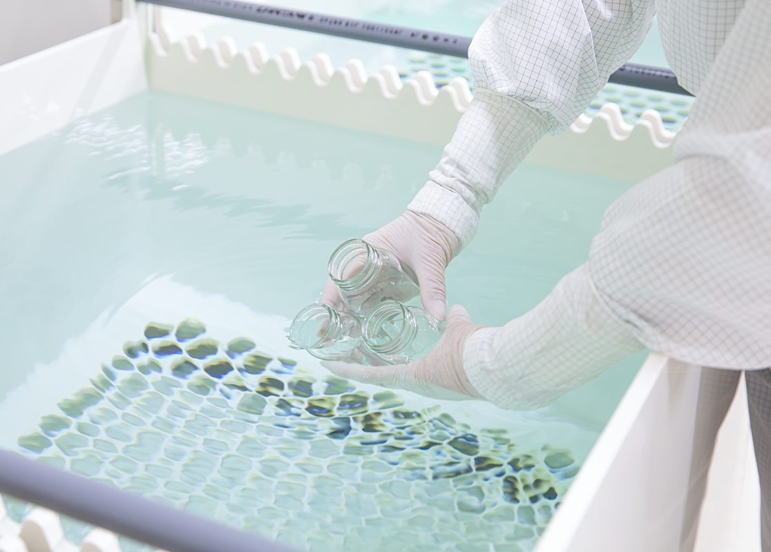 クリーンルームで瓶を洗浄している手元